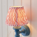 Endon Bevbury Ripple wall light with a blue turned wooden spindle, brass B22 lamp holder and pink pleated faux linen shade with rippled print.