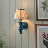 Endon Bevbury Ikat wall light with blue turned wood spindle and tapered pleated ikat shade, mounted on panelled wall beside botanical prints.