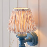 Endon Bevbury Ikat wall light with blue turned wood spindle, brass B22 holder and pleated pink ikat-print shade, mounted on white panelling.