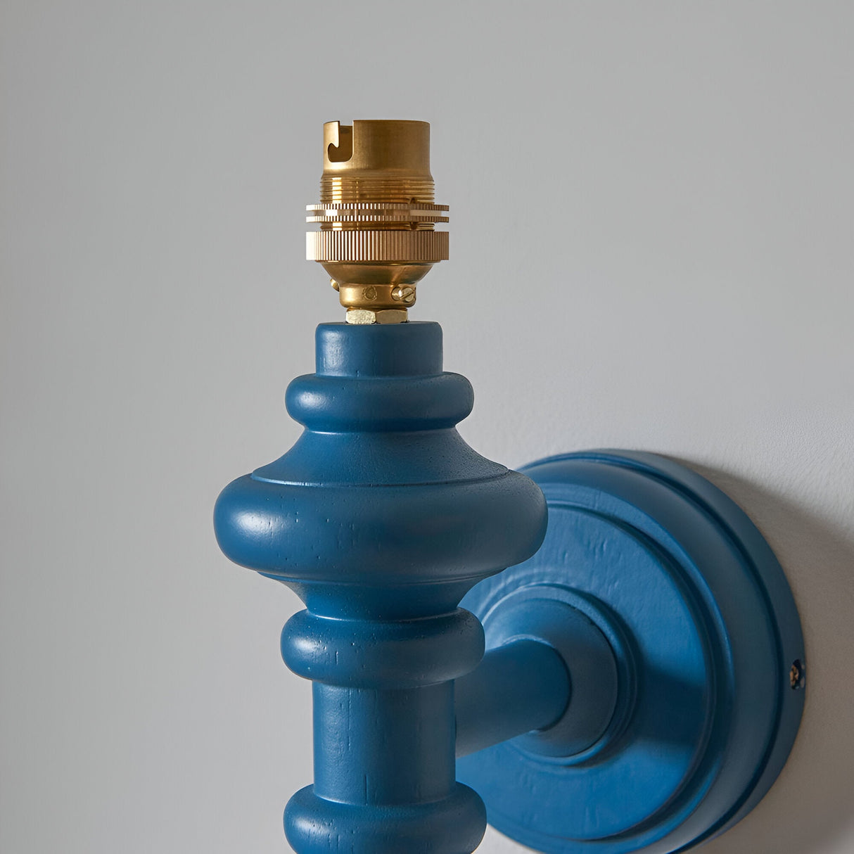 Endon Bevbury Ikat wall light close-up showing the blue turned wooden spindle, round wall plate and brass B22 lamp holder against a pale wall.
