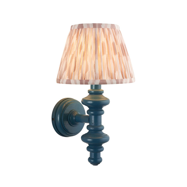 Endon Bevbury Ikat wall light with turned blue wooden spindle, brass B22 holder and tapered pleated pink ikat faux silk shade on a white background.