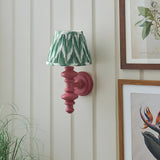 Endon Bevbury Zigzag wall light with a pink turned wooden spindle and pleated green zigzag shade, mounted on white panelling beside framed botanical prints.