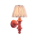 Bevbury Ikat wall light with a coral-painted turned wooden spindle base and pleated ikat-patterned fabric shade, shown on a plain white background.