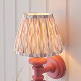 Bevbury Ikat wall light with pink turned wooden spindle base and pleated natural Ikat fabric shade, mounted on a light panelled wall.