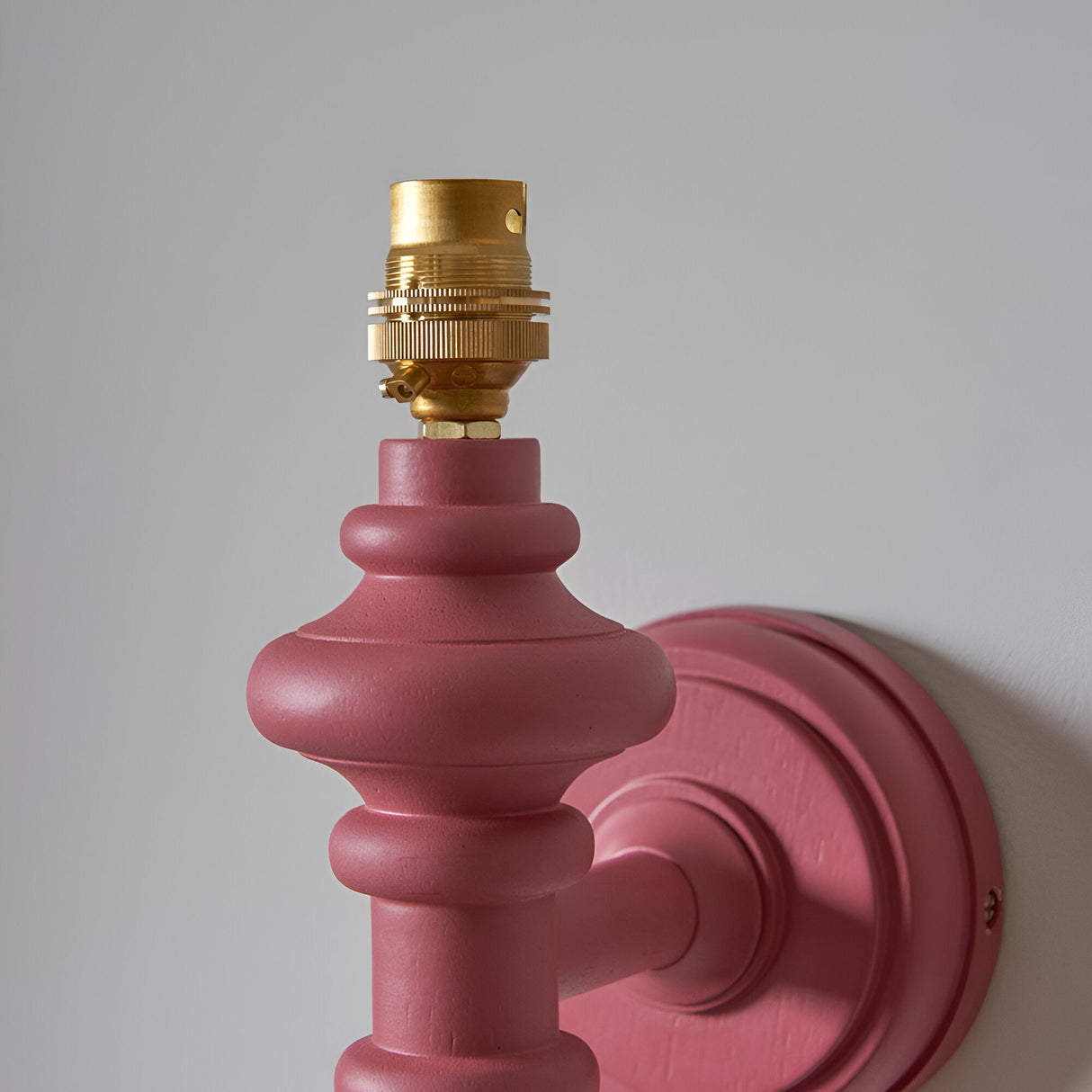 Bevbury Ikat wall light with turned wooden spindle in pink, brass B22 lamp holder, and matching wall bracket, shown against a plain grey background.