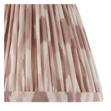 Close-up of the Bevbury Ikat wall light's pleated tapered shade in pink and natural faux silk with a brass-toned trim.