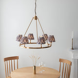 Endon Bevford Zigzag six-light pendant with aged brass hoop frame and pleated grey zigzag fabric shades, hung above a wooden dining table.