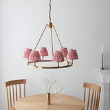 Bevford Ikat 6 Light Pendant in antique brass with coral pink pleated fabric shades on a circular hoop frame, shown above a dining table in a light room.