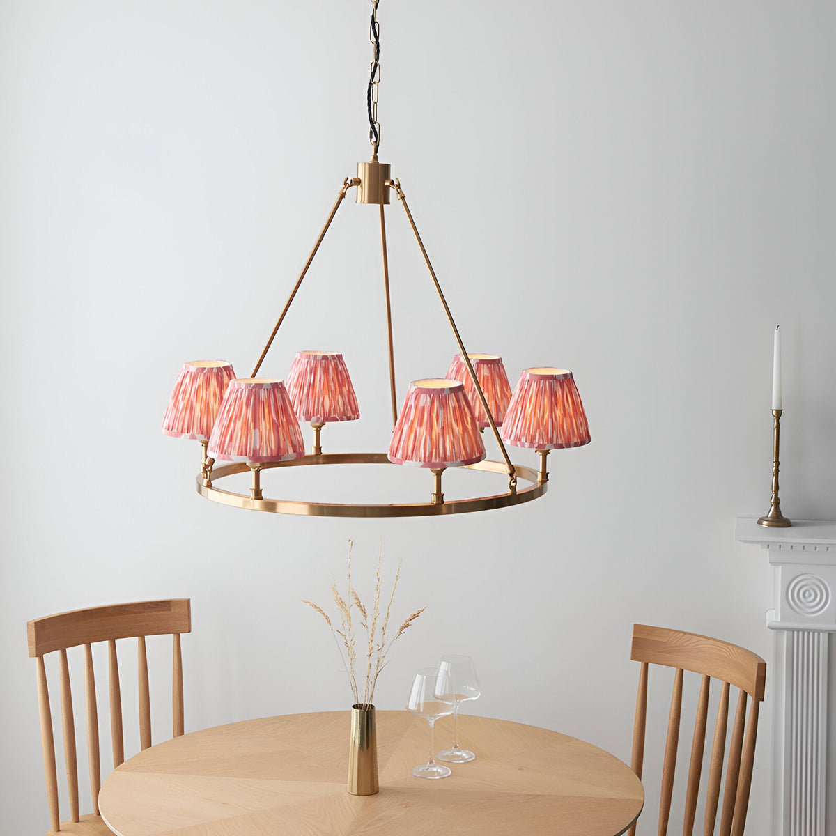 Bevford Ikat 6 Light Pendant in Coral, a circular aged brass hoop chandelier with pleated coral pink fabric shades, shown above a dining table.