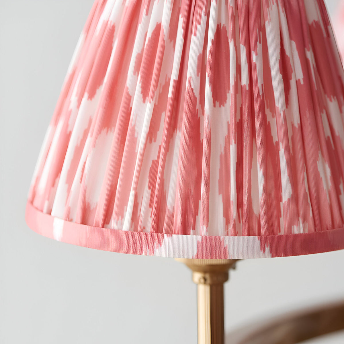 Close-up of Bevford Ikat 6 Light Pendant in coral, showing a pleated fabric shade with pink Ikat pattern, taped hem edge, and brass fitting on light background.