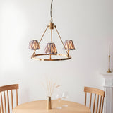 Bevford Zigzag 3-light hoop pendant in aged brass with pleated grey Zigzag fabric shades, shown hanging above a wooden dining table.
