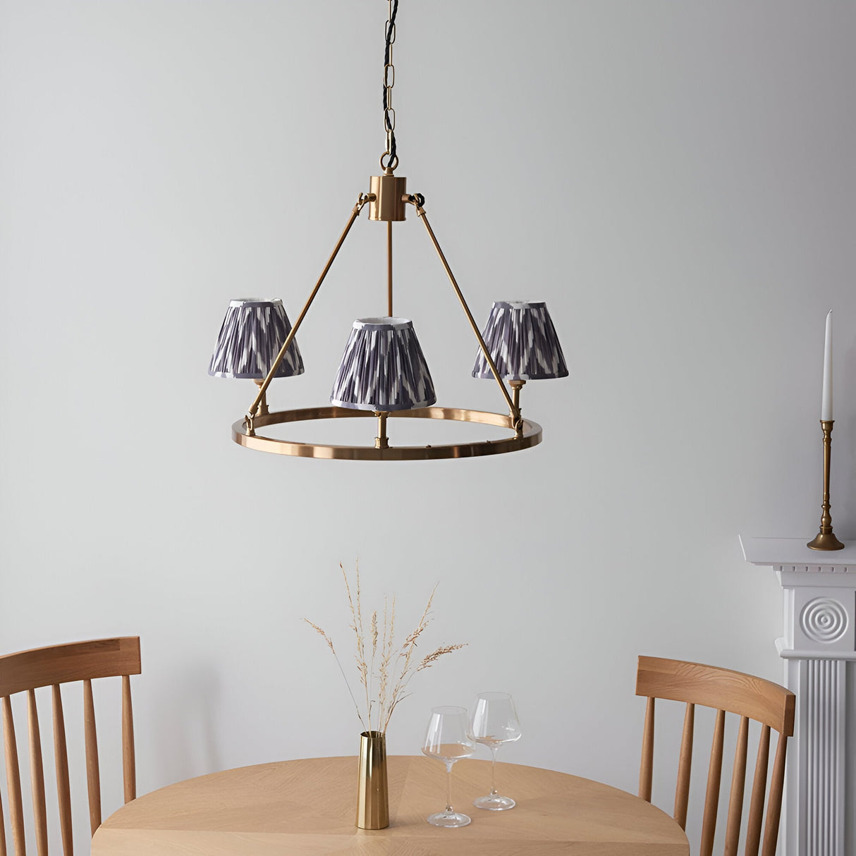 Bevford three-light hoop pendant in aged brass with pleated grey Zigzag fabric shades, shown hanging above a dining table in a neutral room.