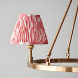 Bevford Ikat 3 Light Pendant in coral, close-up of a pleated fabric shade on an aged brass hoop frame with matching lamp holder, plain grey background.