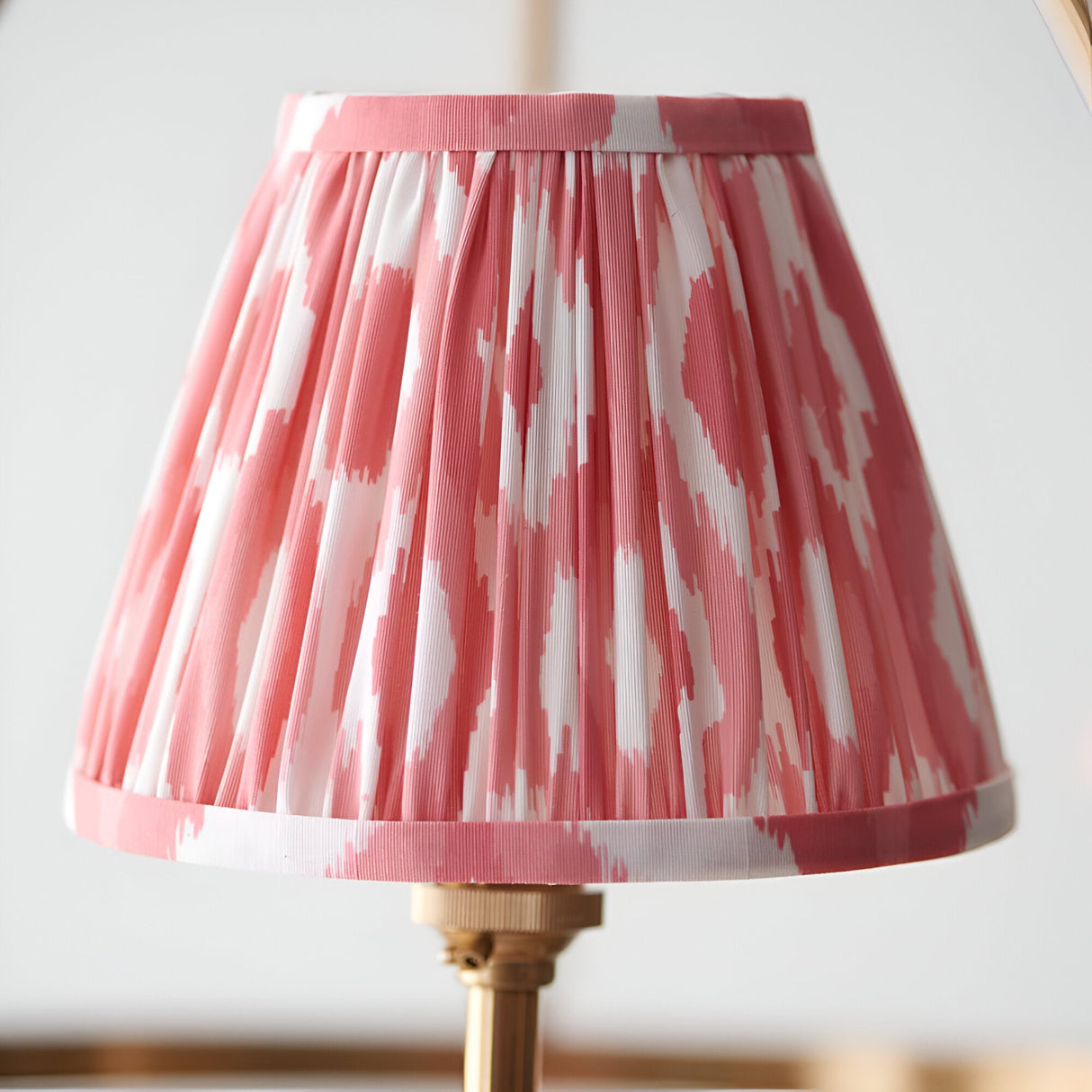 Close-up of a Bevford Ikat 3 Light Pendant shade in pleated coral pink and white fabric, showing a brass gathered trim against a plain light background.