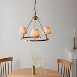 Endon Bevford 3 light pendant with aged brass hoop and peach pleated fabric shades, hung above a wooden dining table in a neutral room.