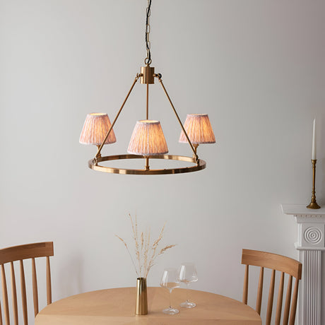 Endon Bevford 3 light pendant with aged brass hoop and peach pleated fabric shades, hung above a wooden dining table in a neutral room.