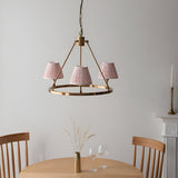 Endon Bevford 3 Light Pendant in aged brass with a circular hoop and three peach pleated fabric shades, shown above a wooden dining table.