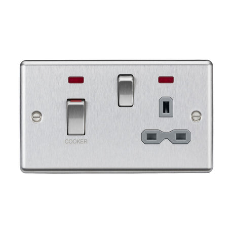 The 45A DP Switch & 13A Socket Neons in brushed chrome, featuring a grey insert and rounded edge, includes a switch labeled COOKER, an additional switch, and a three-pronged power socket. Two red indicator lights are positioned above the switches, enhancing its sleek and modern design typical of cooker control units.