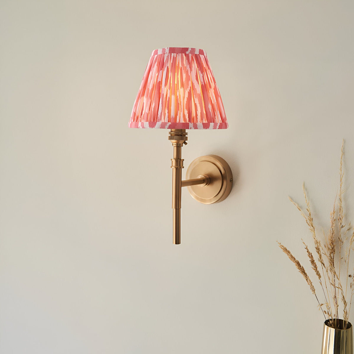 Endon Bevford Ikat wall light with aged brass hoop frame and pleated coral pink ikat print faux silk tapered shade, mounted on a neutral wall.