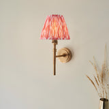 Endon Bevford Ikat wall light with aged brass hoop frame and pleated coral pink ikat print faux silk tapered shade, mounted on a neutral wall.
