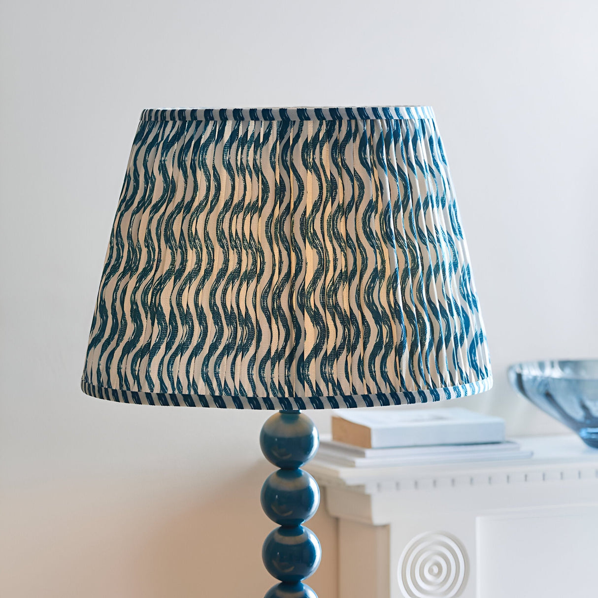Endon Brenleigh floor lamp with pleated blue Ripple print faux linen shade on a stacked marlin blue metal sphere base, beside a white mantel.