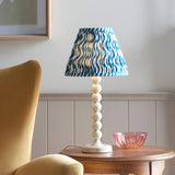 Endon Brenleigh Ripple table lamp with stacked white sphere base and blue and white pleated ripple shade on a wooden side table beside a yellow armchair.
