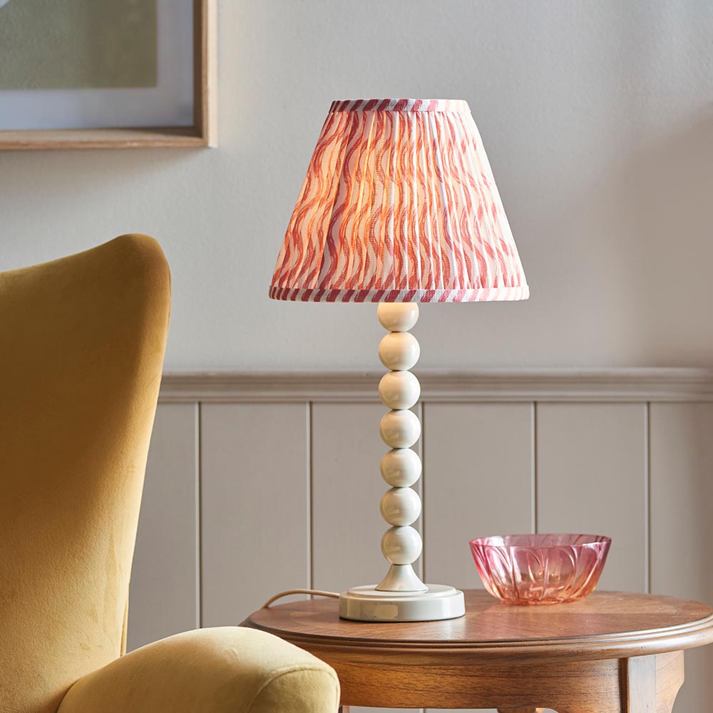 Endon Brenleigh Ripple table lamp with white stacked-sphere base and pink pleated Ripple shade, on a wooden side table beside a mustard chair.