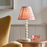 Endon Brenleigh Ripple table lamp with white stacked-sphere base and pink pleated Ripple shade, on a wooden side table beside a mustard chair.