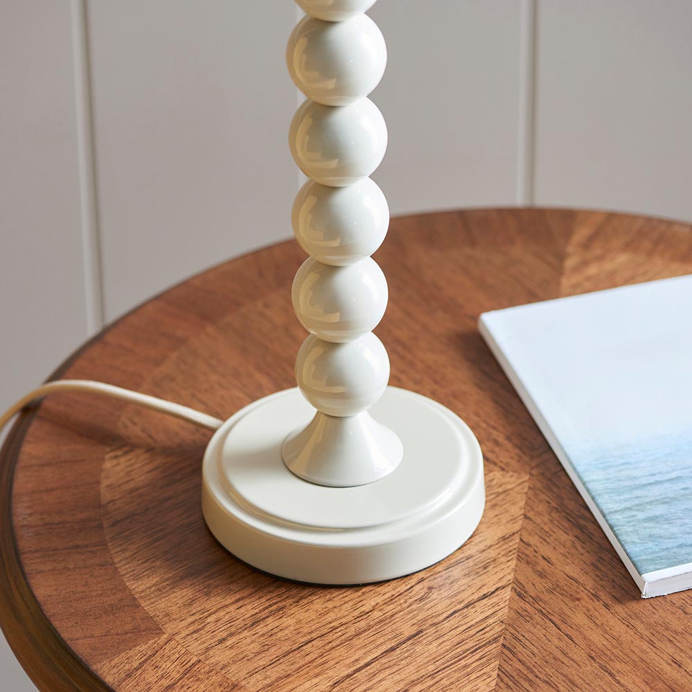 Close-up of the Endon Brenleigh Ripple table lamp base, showing stacked gloss white spheres on a round plinth atop a wooden side table beside a book.