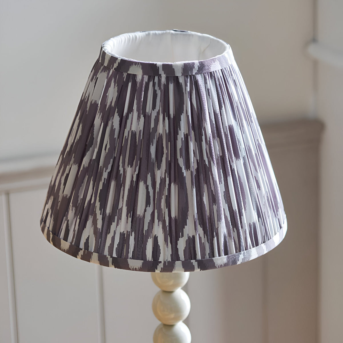 Brenleigh Ikat table lamp with pleated grey and white patterned fabric shade on a white stacked-sphere base, shown against a light neutral background.