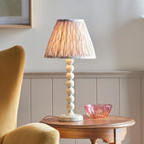 Brenleigh Ikat table lamp with white stacked-sphere base and pleated natural fabric shade, shown on a wooden side table beside a pink glass bowl.