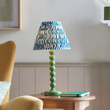 Endon Brenleigh Ripple table lamp with green stacked-sphere base and blue wave-print pleated shade on a wood side table in a living room.