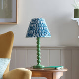 Endon Brenleigh Ripple table lamp with green stacked-sphere metal base and blue wave-print pleated shade on a wooden side table beside a mustard chair.