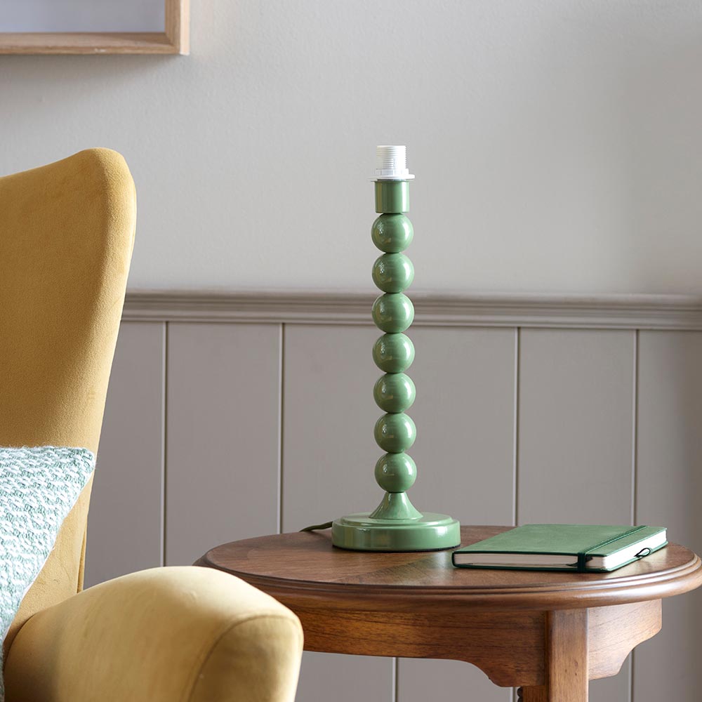 Brenleigh Ikat table lamp base with green gloss stacked-sphere metal stem, shown without shade on a wooden side table beside a green notebook.