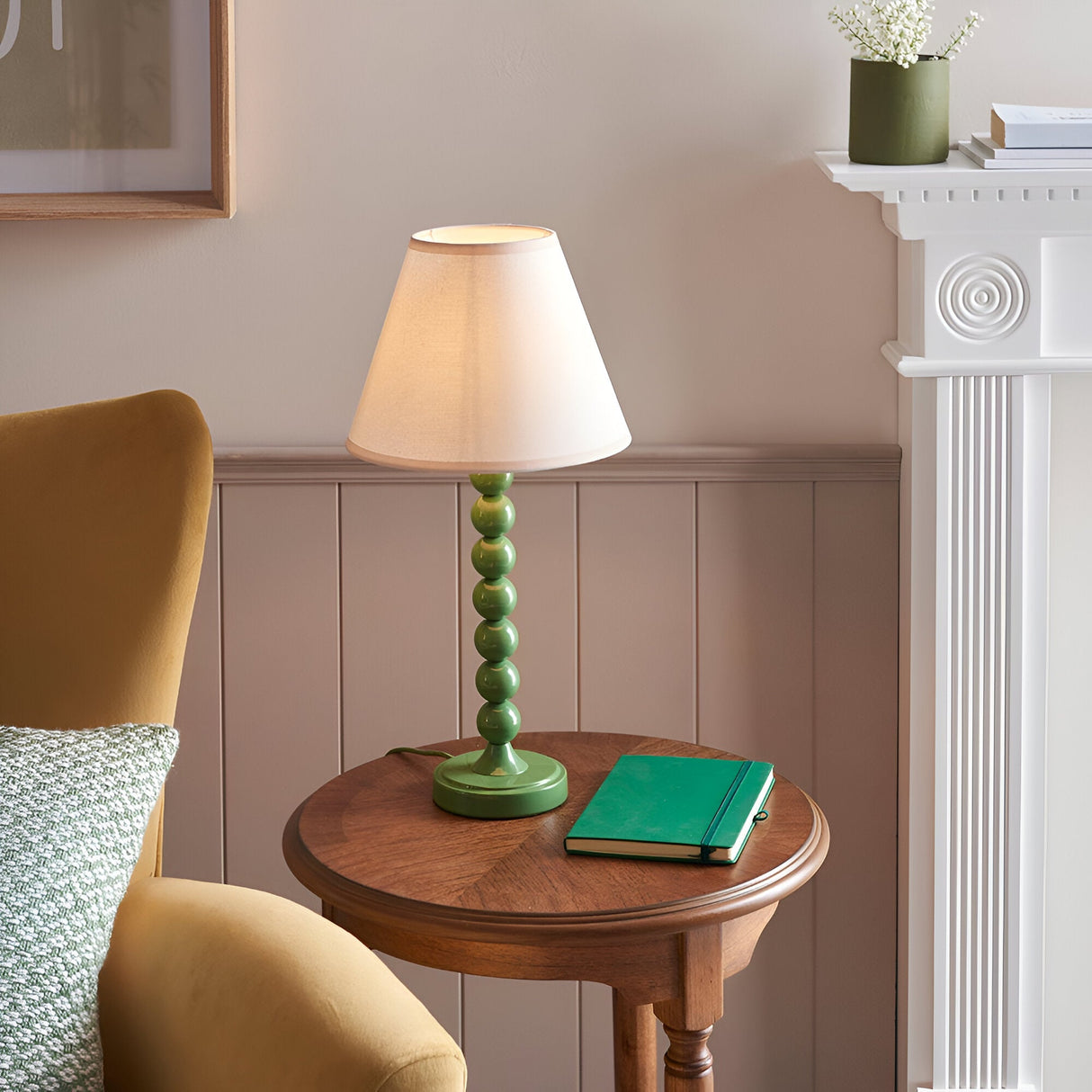 Brenleigh Ivy Table Lamp with green stacked-sphere metal base and white fabric shade, styled on a wooden side table beside a green notebook.