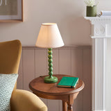 Brenleigh Ivy Table Lamp with green stacked-sphere metal base and white fabric shade, styled on a wooden side table beside a green notebook.