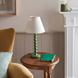Brenleigh Ivy Table Lamp with green stacked-sphere metal base and white fabric shade, styled on a side table beside a notebook.