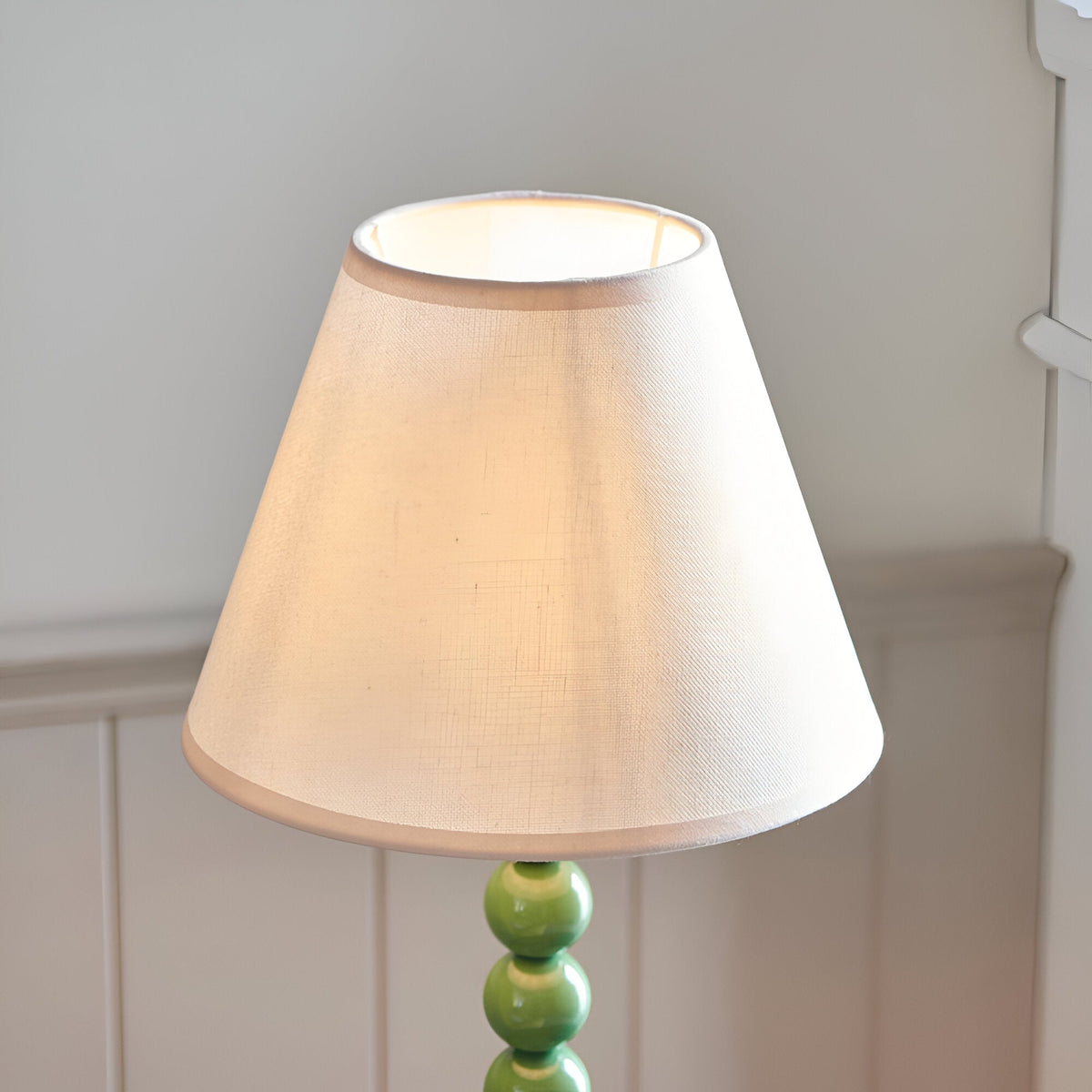 Brenleigh Ivy Table Lamp with white cotton-mix Ivy shade and green stacked-sphere metal base, shown against a light grey wall setting.