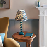 Brenleigh Ripple Table Lamp in blue, with stacked-sphere gloss metal base and pleated wavy-print fabric shade, shown on a side table in a living room.