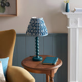 Brenleigh Ripple Table Lamp in blue, with stacked-sphere gloss base and pleated blue and white patterned fabric shade, shown on a side table in a living room.