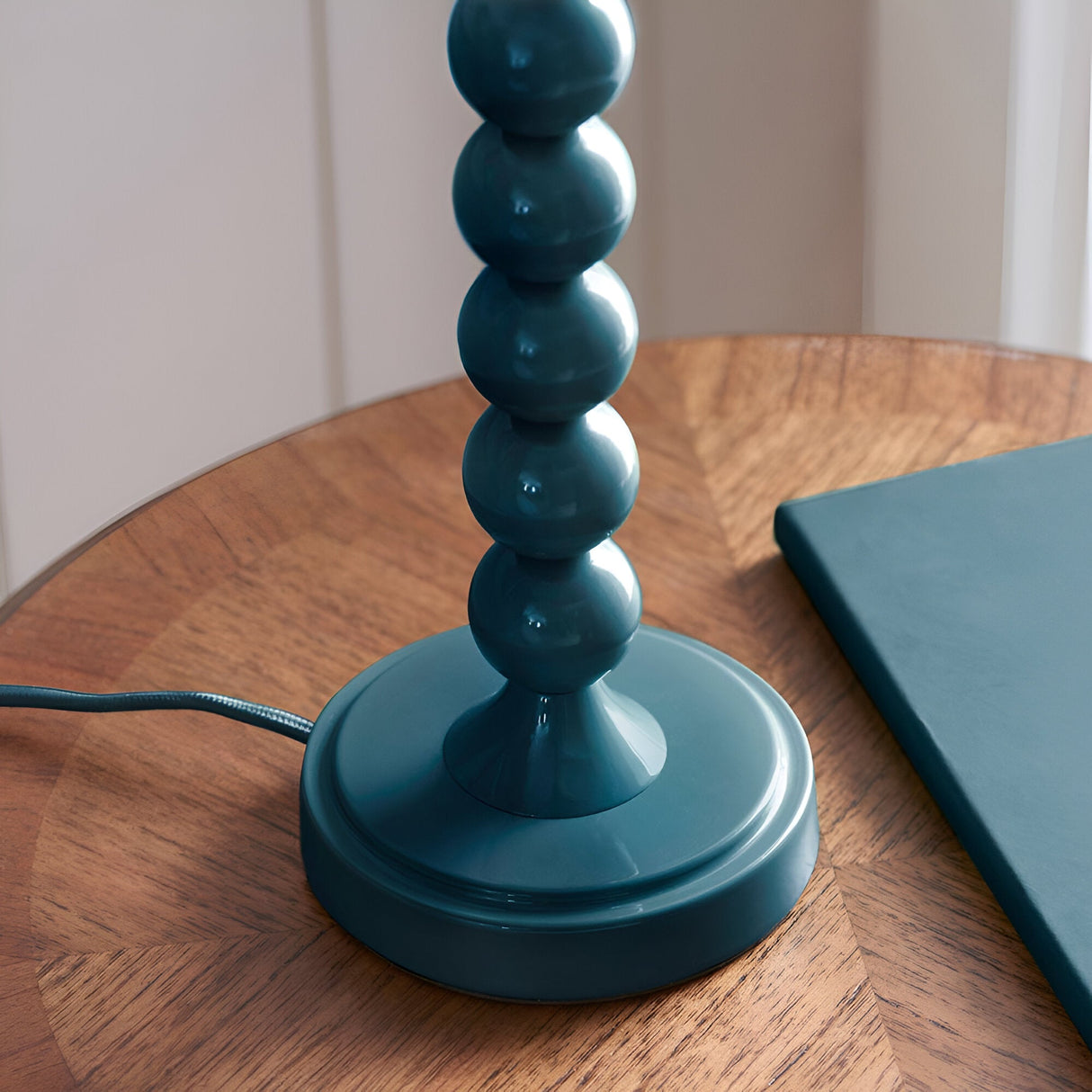 Close-up of the Brenleigh Ivy Table Lamp's teal-blue stacked-sphere metal base and round foot, shown on a wooden table with fabric flex.