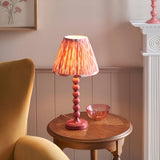 Endon Brenleigh Ikat table lamp with pink stacked-sphere metal base and pleated ikat shade on a wooden side table beside a yellow armchair.