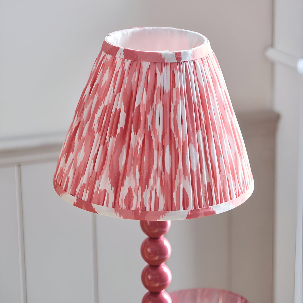 Endon Brenleigh Ikat table lamp with a pink stacked-sphere metal base and pleated pink and white ikat faux silk shade, against pale panelling.