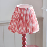 Endon Brenleigh Ikat table lamp with a pink stacked-sphere metal base and pleated pink and white ikat faux silk shade, against pale panelling.