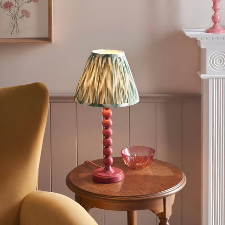 Endon Brenleigh Zigzag table lamp with pink stacked-sphere base and green pleated zigzag shade on a wooden side table beside a mustard armchair.