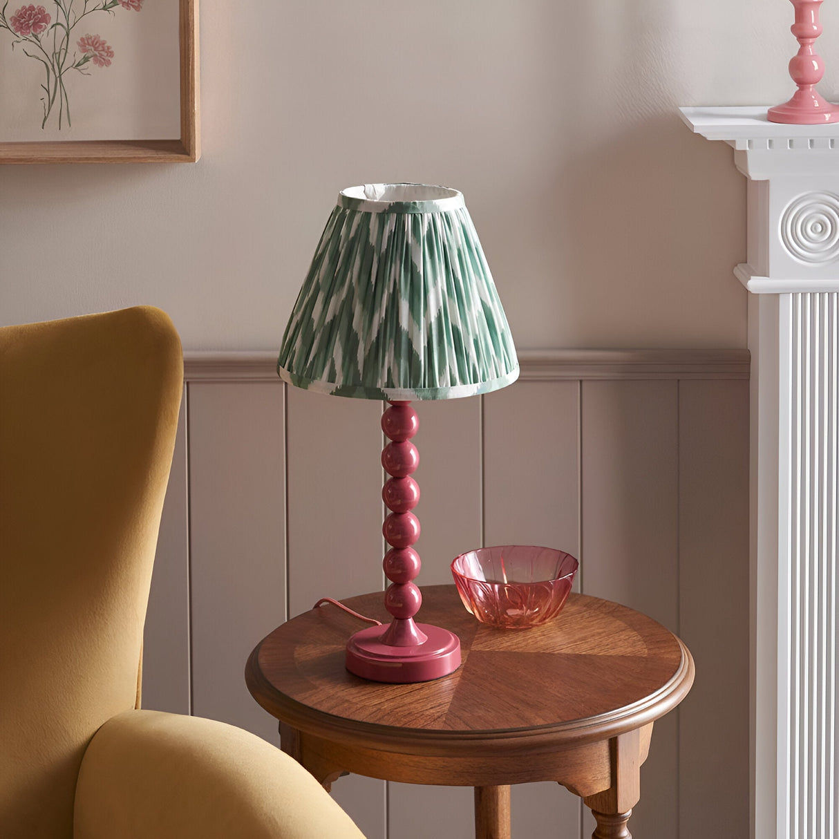 Endon Brenleigh Zigzag table lamp with pink stacked-sphere base and green pleated zigzag shade on a wooden side table beside a mustard armchair.