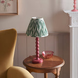 Endon Brenleigh Zigzag table lamp with pink stacked-sphere base and green pleated zigzag shade on a wooden side table beside a mustard armchair.
