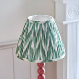 Endon Brenleigh Zigzag table lamp with a pleated green and white chevron faux silk shade on a glossy pink stacked-sphere base, beside white panelling.
