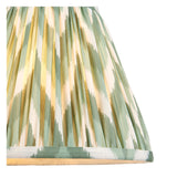 Close-up of the Endon Brenleigh Zigzag table lamp's handmade pleated faux silk shade in green and cream ikat print, illuminated to show the soft glow.