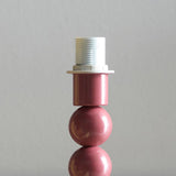 Close-up of the Brenleigh Zigzag Table Lamp's pink gloss stacked-sphere metal base with white threaded E14 bulb fitting, shown against a plain grey background.